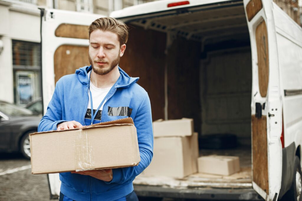 A young delivery man carrying a package near an open delivery truck in the city street.